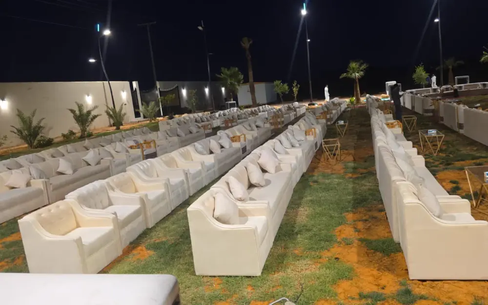 صفوف طويلة من الكنب الأبيض على العشب ليلًا تحت إضاءة الشارع، لمناسبة كبيرة