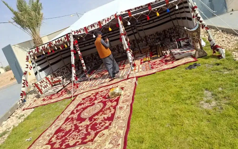 فريق يركّب بيت شعر تراثيًا على أرض عشبية فوق سجاد أحمر