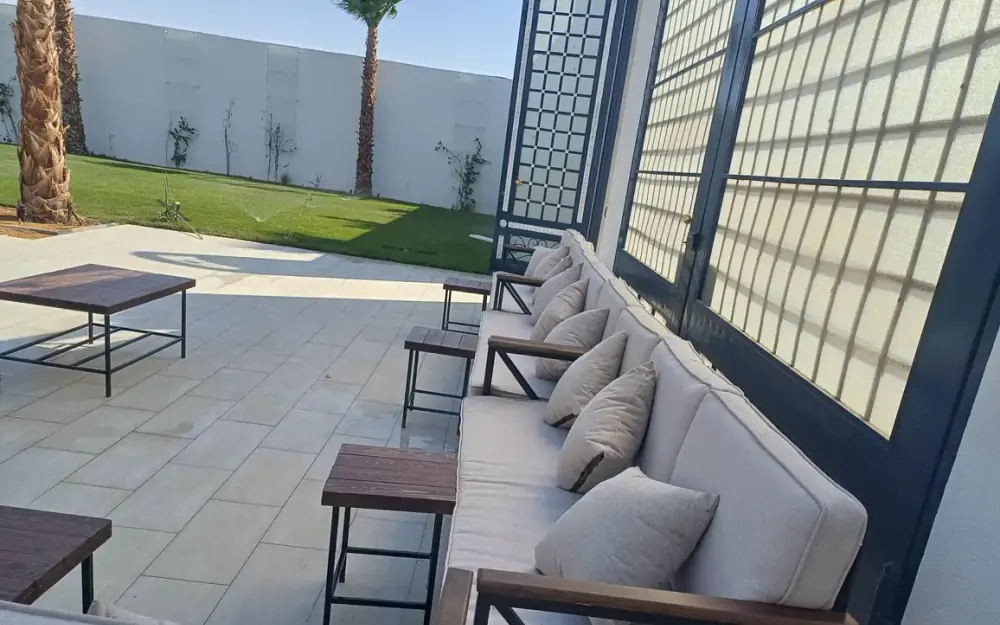 جلسة خارجية بكنب فاتح اللون ووسائد على فناء منزل بجانب مبنى حديث